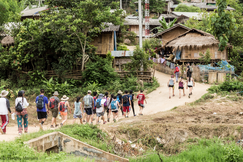 A group of people walking down a dirt road in a village.