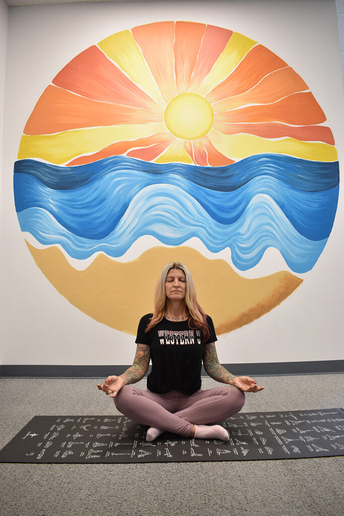 A woman meditating in front of a mural.